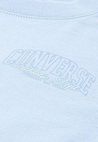 Svetle modré bavlněné tričko s vroubkovaným výstřihem, na přední straně se velkým bílým potiskem "CONVERSE Athletic Dept". Texturovaná tkanina.