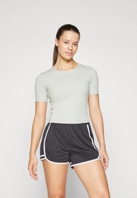 Lys grønn kortermet tettsittende topp med rund hals, kombinert med svarte treningsshorts med hvite sidestriper og elastisk midje.