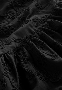Tissu noir avec une broderie florale complexe, présentant une surface texturée et des détails froncés. Richement détaillé avec du fil foncé.