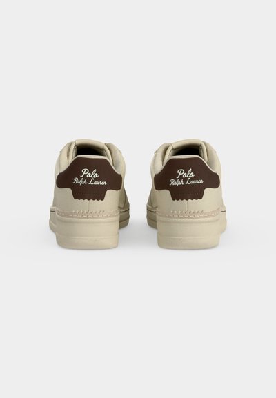 Ζευγάρι μπεζ χαμηλά sneakers με καφέ ταμπά απολήξεις στη φτέρνα που φέρουν λευκή σήμανση Polo Ralph Lauren, εμφανιζόμενα από πίσω σε απλό φόντο.