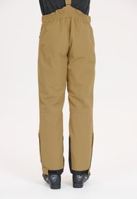 Bruine waterdichte broek met verstelbare banden, elastische taille en zijritsen bij de zoom, gedragen met zwarte laarzen. Soepele textuur.