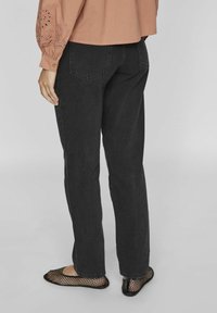 Pantalones de mezclilla negros con un corte recto, que cuentan con dos bolsillos traseros, combinados con bailarinas de malla negras. La parte superior es una blusa de color durazno.