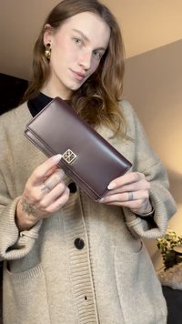 Brown leather wallet with a gold geometric logo. Features a sleek design, smooth texture, and a flap closure.