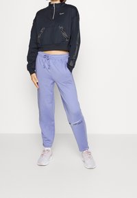 Marineblaues kurzgeschnittenes Sweatshirt mit halbem Reißverschluss und Fronttasche, kombiniert mit hellvioletten Jogginghosen mit elastischem Bund und dem aufgedruckten Schriftzug "JUST DO IT".