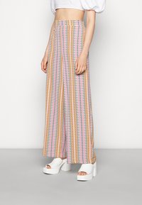 Vida byxor med hög midja, prydda med ett flerfärgat zigzag-mönster i rosa, gult och blått. Tillverkade av lättviktsmaterial.