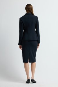 Námořnický saka s tvarovanými rameny, peplum pasem a zlatými knoflíky, kombinované s přiléhavou tužkovou sukní ke kolenům s rozparkem vzadu.