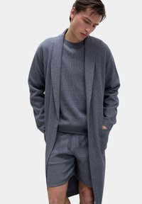 Rrobe grigio testurizzato indossato sopra una felpa e pantaloni corti abbinati di colore grigio, con tasche profonde e una vestibilità comoda. Tessuto morbido, design minimale.