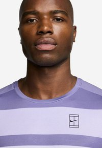 Lilla stripete treningstrøye med teksturert overflate. Har sort Nike-logo på brystet, rund hals og korte ermer.