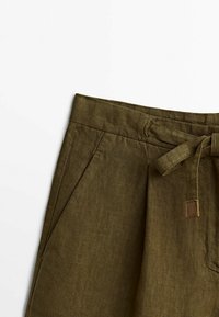 Shorts in lino verde oliva con vita piatta, passanti per cintura e un laccio in tessuto. Presentano tasche laterali e una piccola etichetta in pelle marrone.