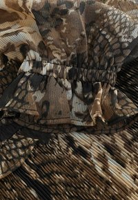 Tissu léger et fluide dans des teintes de marron avec un design texturé plissé. Présente un poignet froncé et des accents décoratifs ressemblant à un imprimé animal.