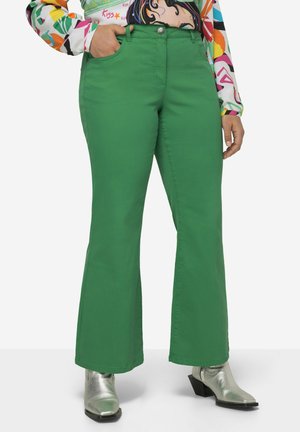 Vaqueros verdes acampanados de textura suave, con bolsillos frontales y cierre de botón. Combinados con botas de tobillo metálicas para un contraste.
