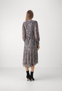 Robe longue imprimée python dans des nuances de gris et de beige. Manches longues transparentes, taille cintrée et ourlet superposé, assortie à des bottines noires.