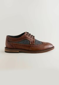 Chaussure en cuir marron avec tissu en chevron gris, détails brogue, bout rond et lacets noirs. Talon en bois plat avec des accents cousus.