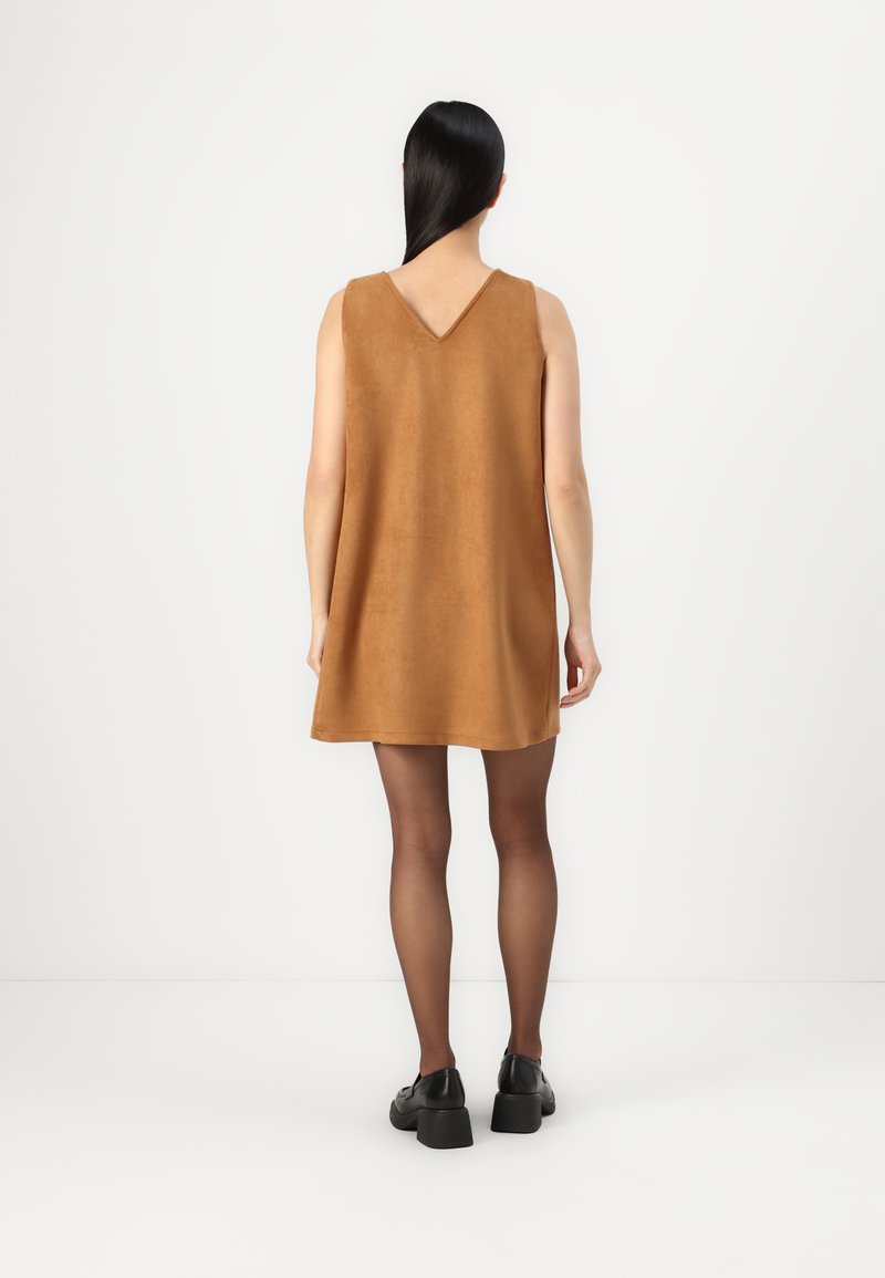 Beige ärmelloses Kleid mit V-förmigem Rücken und lockerer Passform, aus weichem Stoff gefertigt, kombiniert mit glänzenden schwarzen Schuhen.