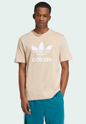 Camiseta de algodón beige con un logo trefoil de Adidas en blanco y rayas horizontales. Cuello redondo, mangas cortas y un corte relajado.