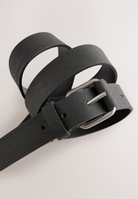 Cintura nera in pelle con finitura testurizzata, con fibbia in metallo argento e fori regolabili per la misura, arrotolata in una forma sovrapposta.