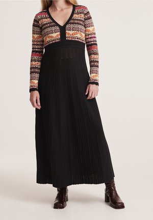 Robe maxi avec un haut à motifs dans des couleurs vives et une longue jupe plissée noire. Elle présente un col en V et des manches longues ; tissu en tricot texturé.