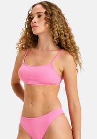 Růžový texturovaný bikini top se zavazováním na tenké ramínka, v kombinaci s odpovídajícími nízkými bikini spodky. Hladká látka s mírným leskem.