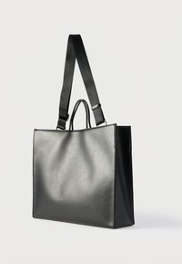 Μαύρη ορθογώνια δερμάτινη τσάντα tote με δύο κοντά χερούλια και ένα ρυθμιζόμενο μακρύ λουρί ώμου, φωτογραφημένη σε απλό φόντο.