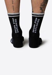 Calcetines de rayas negras con el texto blanco "NUNCA DEJES DE EXPLORAR" en los lados, con un puño de rayas blancas. Material textil suave.