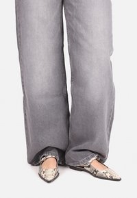Vaqueros de pierna ancha gris y zapatos planos de punta afilada con un estampado de serpiente en blanco y negro. Los materiales parecen ser denim y sintético texturizado.