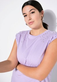 Helllila kurzärmliges Oberteil mit dekorativen Nieten an den Schultern. Weicher Stoff mit lockerer Passform und Rundhalsausschnitt.