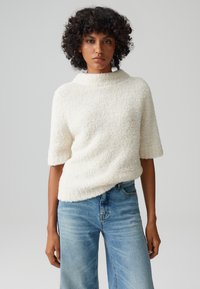 Maglione a maglia con trama, di colore crema, con colletto alto e maniche corte, abbinato a jeans a gamba larga di colore blu chiaro. Tessuto morbido, vestibilità comoda.