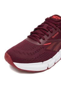 Bordo värvi spordijalats hingava võrgukattega pealmise osa, tekstureeritud detailide ja Reeboki logoga, millel on paks valge tald ning kontrastsed punased aktsendid.