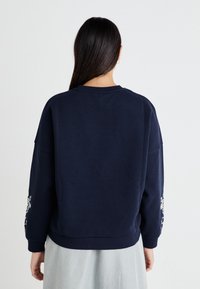 Sudadera azul marino hecha de una mezcla de algodón, con corte relajado, mangas largas y bordado floral en el brazo derecho.