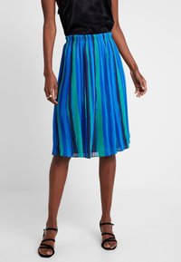 Plisowana spódnica midi w paski w kolorach niebieskim, zielonym i czarnym. Elastyczny pas i lekki, zwiewny materiał. Noszona z czarnymi sandałami na paski.