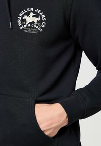 Black hoodie made from soft fabric, featuring a front pocket, ribbed cuffs, and a white and gold logo with a horse design.