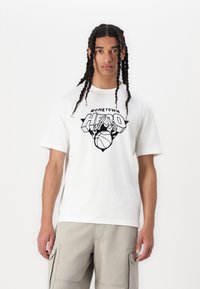 Hvid bomulds t-shirt med et sort grafisk design med teksten "HOMETOWN HERO" og en basketball, sat mod en ensfarvet baggrund.