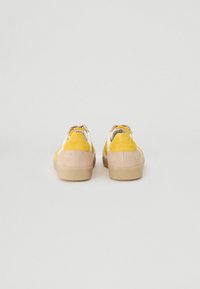 Sneakers in suede giallo e beige con dettagli bianchi, tallone arrotondato, suola piatta e lacci grigi. Presentano una tomaia texturizzata.