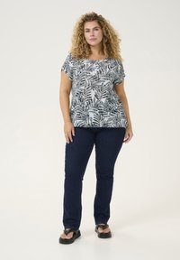 Top con stampa floreale in blu chiaro e blu scuro, presenta maniche corte e vestibilità rilassata. Abbinato a jeans blu scuro e sandali neri.
