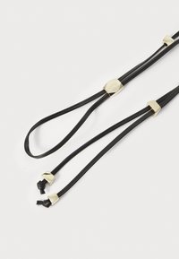 Correias de couro pretas com detalhes em metal dourado. O design apresenta dois cordões longos e finos com extremidades bem atadas e uma textura suave.