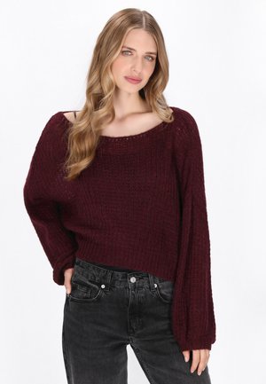 Bordeaux gebreide trui met een losse, cropped pasvorm, brede boot halslijn en geribbelde textuur. Gecombineerd met zwarte high-waisted spijkerbroek.