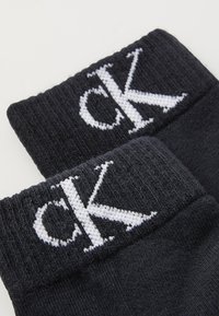 Čierne bavlnené ponožky s rebrovanými manžetami a bielym vyšitým logom "ck". Mäkkoštruktúrované; navrhnuté pre pohodlie a každodenné nosenie.