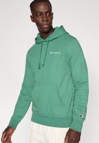 Πράσινο φούτερ με κουκούλα από μείγμα βαμβακιού, με τσέπη καγκουρό, κουκούλα με κορδόνι και κεντημένο λογότυπο στο στήθος. Ριμπ μανσέτες και τελείωμα.