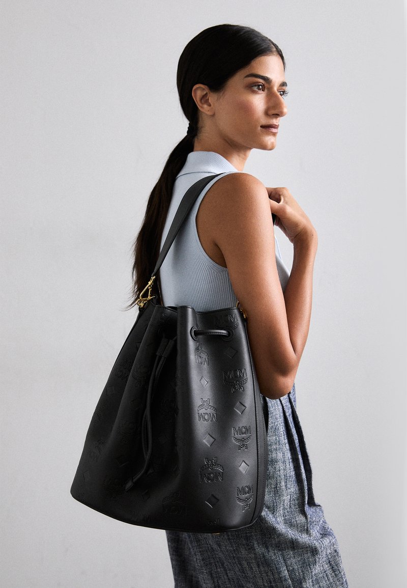 Borsa a secchiello nera in pelle con loghi in rilievo, chiusura con coulisse e dettagli in hardware dorato. Include una superficie testurizzata e una base rotonda.