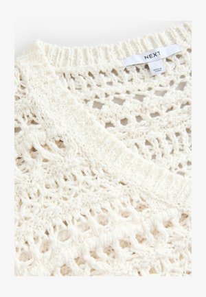 Kreemivarvi kootud sviiter, millel on lahtine ja avatud kudumise disain ning soonikuline kaelus. Sildil on tekst "NEXT."