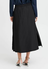 Jupe midi noire au tissu lisse, dotée de fentes latérales et d'une taille élastique. Assortie à des sandales à talons hauts en argent.