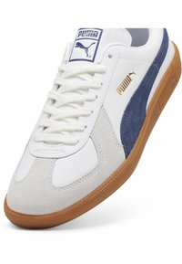 Weißer Sneaker mit marineblauen Wildlederakzenten, strukturierter Gummisohle und goldenen Logodetails. Verfügt über weiße Schnürsenkel und ein abgerundetes Zehendesign.