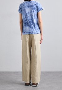 Camiseta de tie-dye azul con mangas cortas, combinada con pantalones de pierna ancha beige. El conjunto presenta un corte relajado y una textura de tela suave.