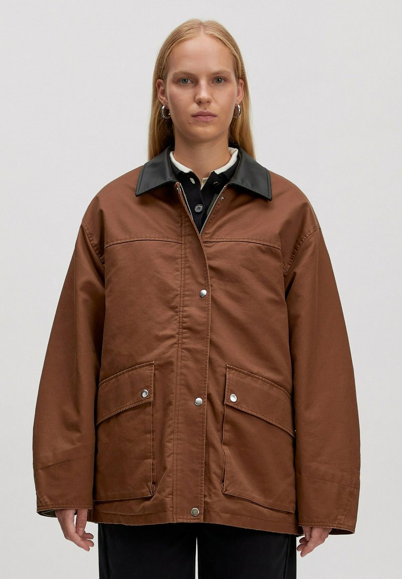 Bruine oversized jas van textiel met een zwarte neplederen kraag, voorzien van twee vo pockets en drukknoopsluitingen.