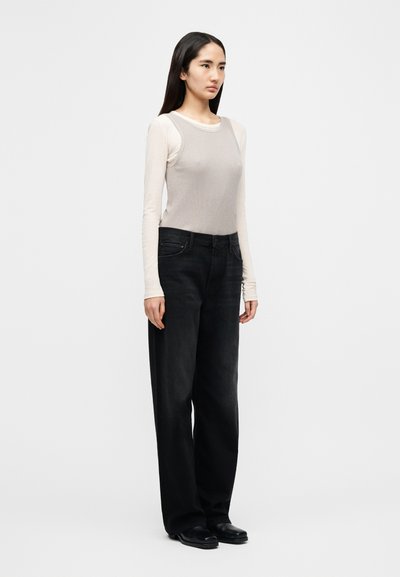 Φωτεινή μπεζ μπλούζα με μακριά μανίκια και ριμπ ύφανση, συνδυασμένη με φαρδιά μαύρα τζιν παντελόνια με πλαϊνές τσέπες και ίσια γραμμή. Ολοκληρώνεται με απλά μαύρα παπούτσια.