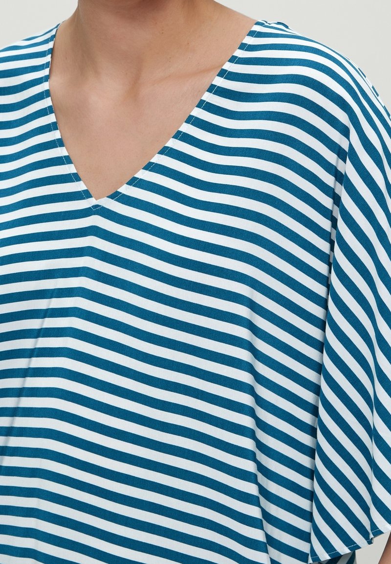 Femme portant un t-shirt à rayures horizontales bleues et blanches avec un col en V, montrant le cou et la partie supérieure de la poitrine.