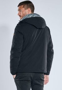Black puffer jacket with a grey lined hood. Features include a smooth texture and a slightly fitted shape. No visible front details.