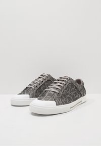 Grijze sneakers met een logo patroon, een bovenwerk van gestructureerd canvas, een ronde rubberen neus en een witte rubberen zool met vetersluiting.