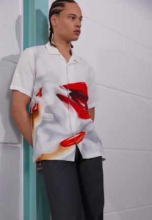 Short-sleeve button-up shirt in lightweight white fabric, featuring abstract red and orange graphic patterns and a relaxed fit.