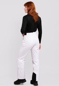 Witte skibroek met een hoge taille, zippers aan de zijkanten en zwarte enkelaccenten, gecombineerd met een zwart langsluiting.